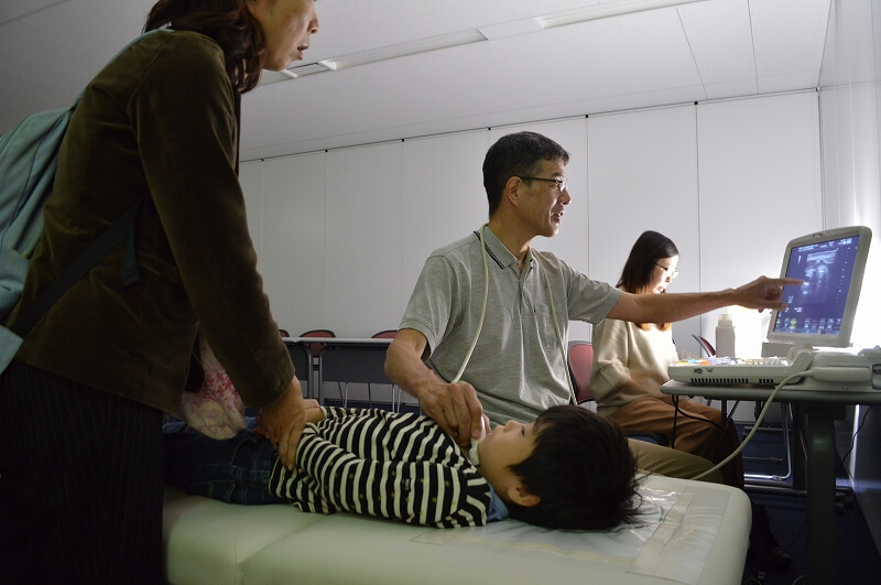 専門医によるエコー検診。はじめは不安そうなお子さんも先生の声かけに安心して受信していました。・甲状腺検診