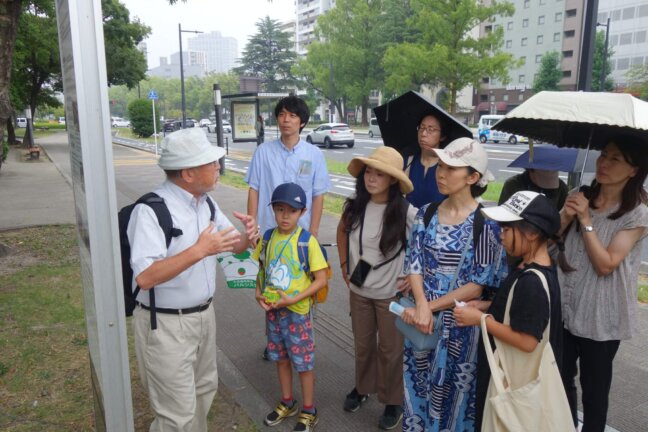 被爆樹木の前で、多賀さんの説明に耳を傾ける参加者